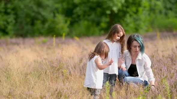 Happy young mom plays with children while sitting on green grass in the field.