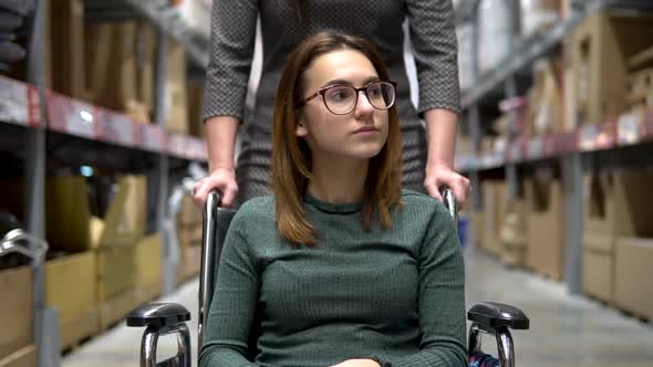 A Young Woman Is Sitting in a Wheelchair, Female Assistant Drives a Woman in a Wheelchair alt