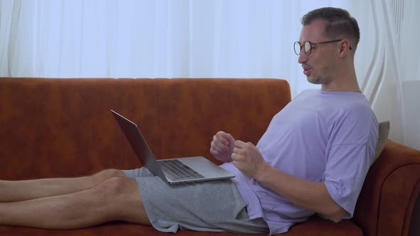 A Man Communicates on a Laptop Via Video Link From Home Lying on the Couch