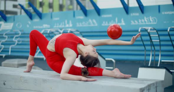 Woman in Red Sports Costume Performing Callisthenics Exercises with Gymnastic Ball at Workout alt