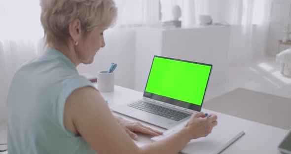 Aged Woman Is Learning Online, Viewing Training Webinar on Green Screen of Laptop for Chroma Key alt