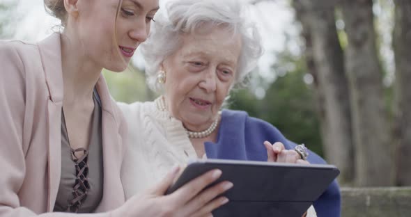Woman and Senior Grandmother Using Tablet Device for Video Call at Park