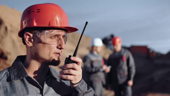 Confident Male Foreman Worker Discussing Using Walkie Talkie in Construction Site at Sunset alt
