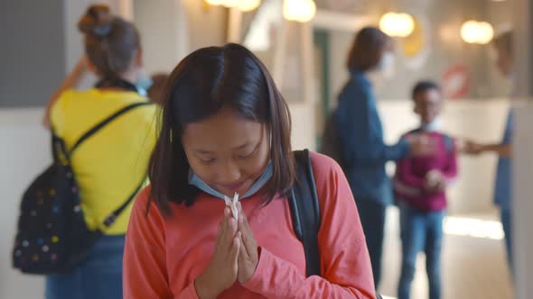 Sick Asian Schoolgirl Sneezing in Paper Tissue Standing in School Corridor alt