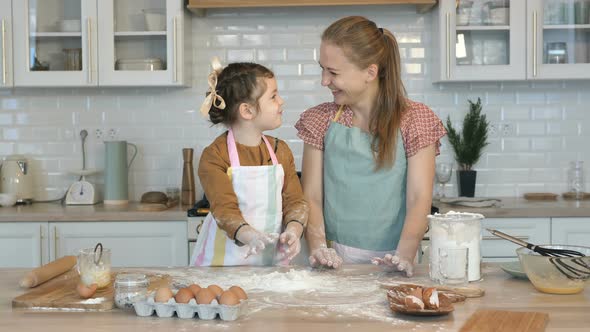 Happy Mother and Daughter Cook Together in the Kitchen, Throw Flour on the Table and Laugh. Have Fun alt