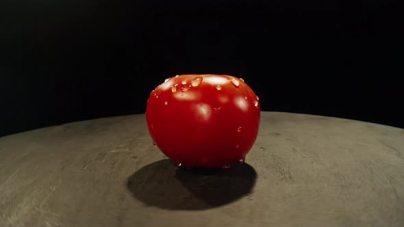 Camera Revolves Around a Red Tomato with Drops of Water on a Table in Dark Room