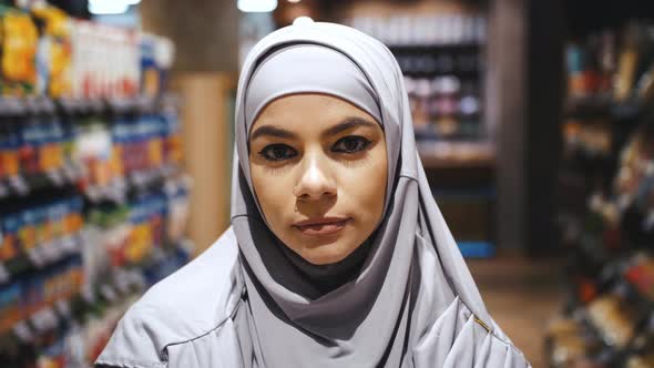 Portrait of Young Beautiful Confident Muslim Woman with Piercing in Hijab in the Supermarket alt