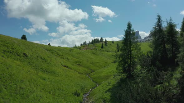 Lush green valley with small mountain stream, Dolomites Italy, aerial alt