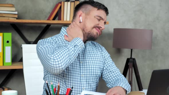 Tired student writes in notebook massaging neck after over work at laptop alt