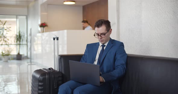 Young Businessman Using Laptop Sitting in Modern Hotel Lobby alt