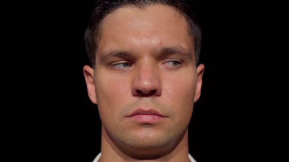 Closeup of an Attractive Young Man's Face Anxiously Watching From Right to Left on Dark Background