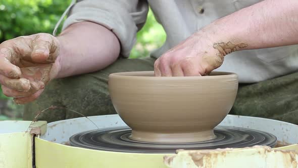 Caucasian Male Potter Removes Moisture with Yellow Sponge From an Earthen Pot on an Electronic alt