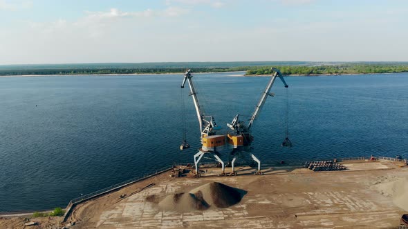 Two Cranes Unloading a Barge Full of Breakstones at Docks alt