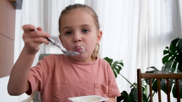 Little Girl Eats Delicious Yogurt for Breakfast at Home alt