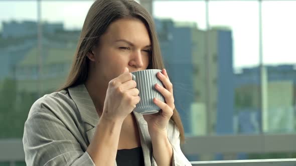 Beautiful Young Businesswoman Drinking Hot Tea or Coffee While Standing on the Office Balcony