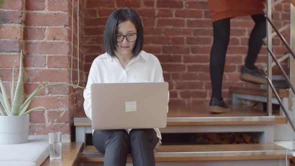 Asian Woman Using Laptop while Sitting on Staircase alt