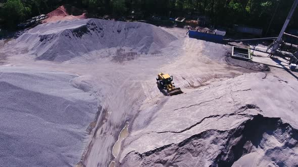 A bulldozer is gaining rubble. The territory of the granite quarry, top view from the copter. alt