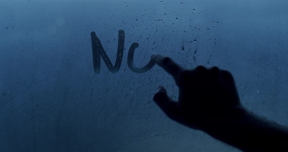 A man's hand writes a No War message on the window with his finger.Stop War text alt