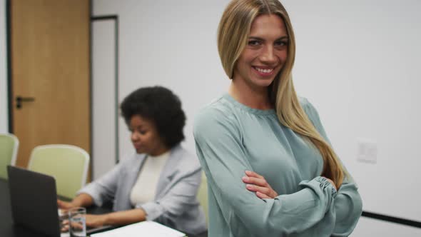 Portrait of caucasian businesswoman smiling in office, with colleague working in background alt