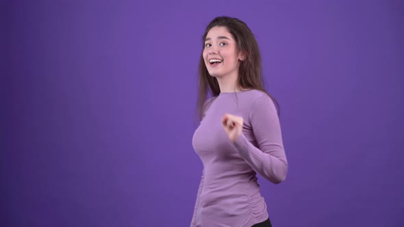 The Charismatic and Optimistic Girl Looks Smiling in Profile Points with Her Index Finger and Blinks alt