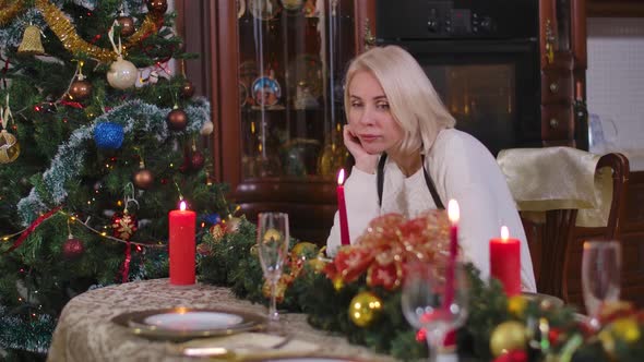 Sad Lonely Young Woman Sitting at Table on Christmas Eve Blowing Out Candles alt