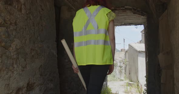 Young female architect or engineer walks down a street between abandoned houses alt
