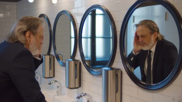 Tired Mature Businessman Standing in Public Restroom Looking Into Mirror alt