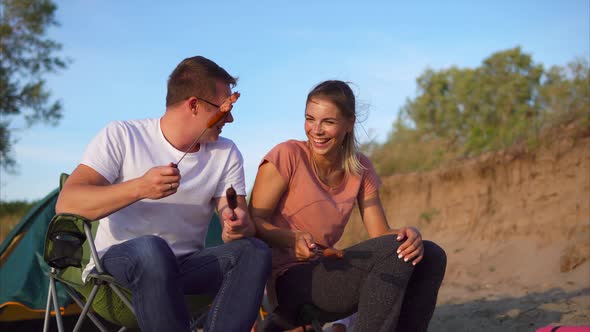 A Loving Couple Talking and Eating Sausages Cooked on Skewers Outdoors