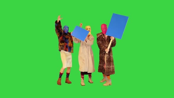 Three Girls in Balaclavas Hold Banners Expressing Protest on a Green Screen Chroma Key
