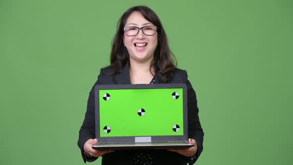 Mature Beautiful Asian Businesswoman Showing Laptop Against Green Background alt