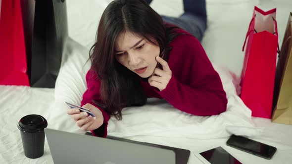 woman thinking and using laptop computer for online shopping with credit card on a bed