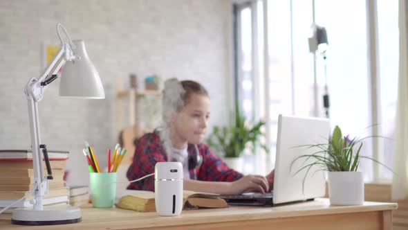 Humidifier on the Table and a Teenager Using the Laptop alt