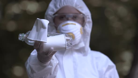 Person in Protective Mask Showing Plastic and Paper Trash, Say Yes to Recycling alt