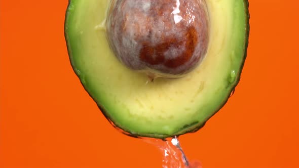 Water falling from avocado on orange background. Avocado slice and water splashing, drops of juice alt