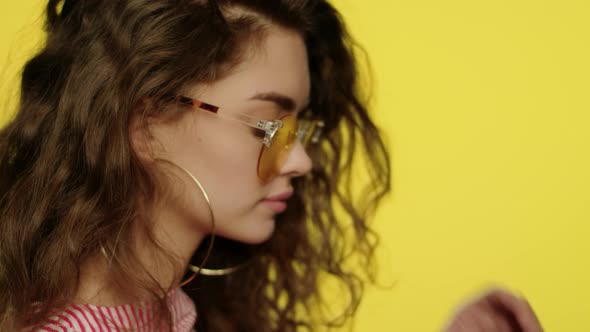 Playful Woman in Yellow Glasses Looking To Camera and Winking Eye in Studio alt