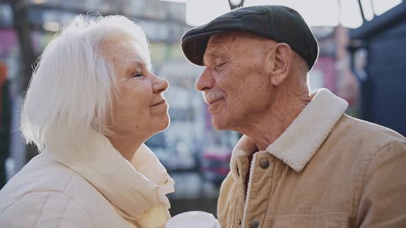 A Stylish Elderly Couple Kiss Standing on a Sunny Modern Street