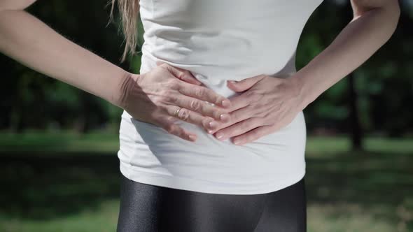 Unrecognizable Slim Caucasian Woman Having Stomach Pain Outdoors. Young Athletic Lady Holding Belly alt