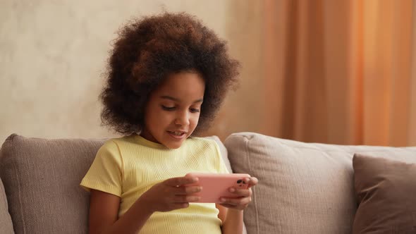 Portrait Little African American Girl in Plays a Game on Smartphone alt