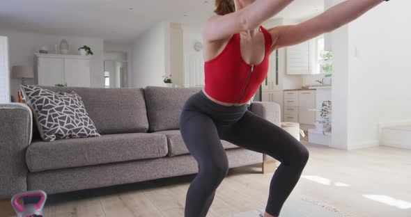 Woman performing squat exercise while using dumbbells at home alt