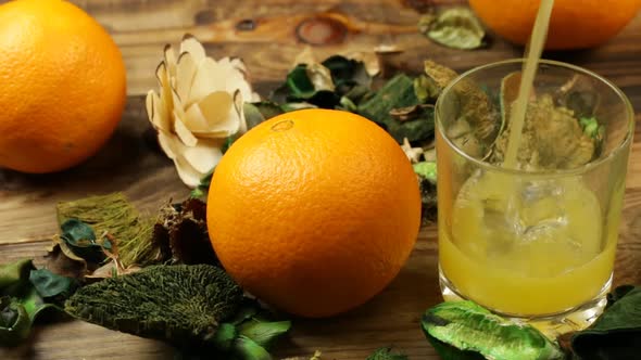 Orange Juice Is Poured Into A Glass On A Table With Flowers And Oranges.