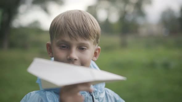 Closeup Portrait of Charming Caucasian Schoolboy Launching Paper Plane Outdoors alt