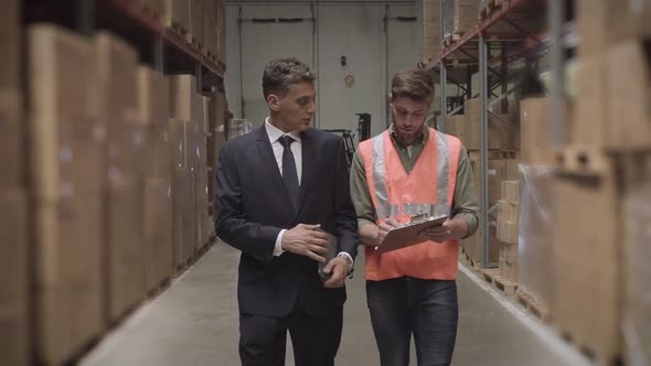 Worker and businessman with digital tablet and clipboard in warehouse alt