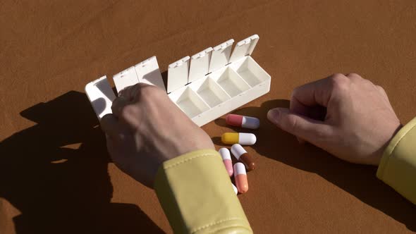 Female hand sorting pills in pillbox on brown background