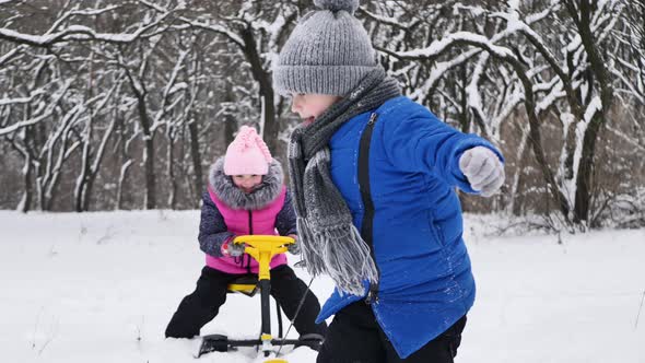 Little Boy Rides a Girl on a Sled in Winter in a Snowcovered Forest