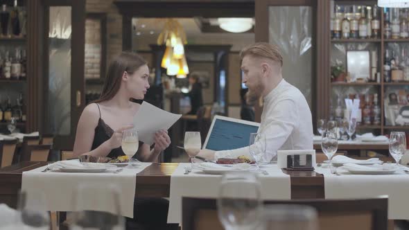 Young Beautiful Woman Sit with Papers on the Table in Restaurant with a Mature Bearded Man alt