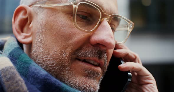 A Grayhaired Man Uses a Mobile Phone Standing in Business Center of the City alt