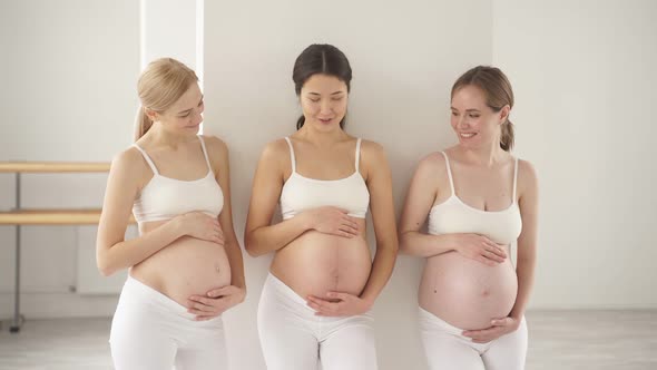 Portrait of Three Attractive Young Pregnant Women Standing in Studio in White Sportive Outfit