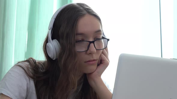 Serious Caucasian Girl Wearing Headphones and Watching an Educational Video Course with Her Laptop alt