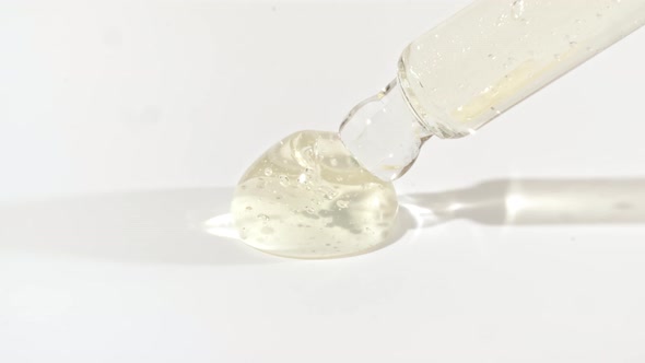Macro Shot of Transparent Yellow Cosmetic Fluid Gel Cream With Bubbles in Pipette Drips on a White alt