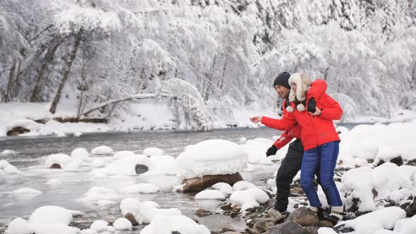 A Young Happy Family Stands at the Mouth of a Mountain River. Couple in Love Throws Pebbles alt